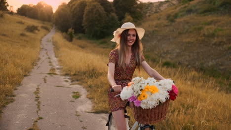 Ein-Mädchen-In-Einem-Kleid-Fährt-Fahrrad-Mit-Blumen-In-Einem-Korb-Und-Genießt-Lachend-Die-Freiheit-Und-Die-Sommerluft.-Zeitlupe.